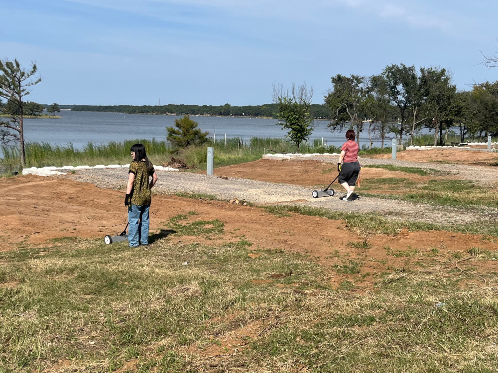 Two students using magnetic rakes to pick up scrap metal.